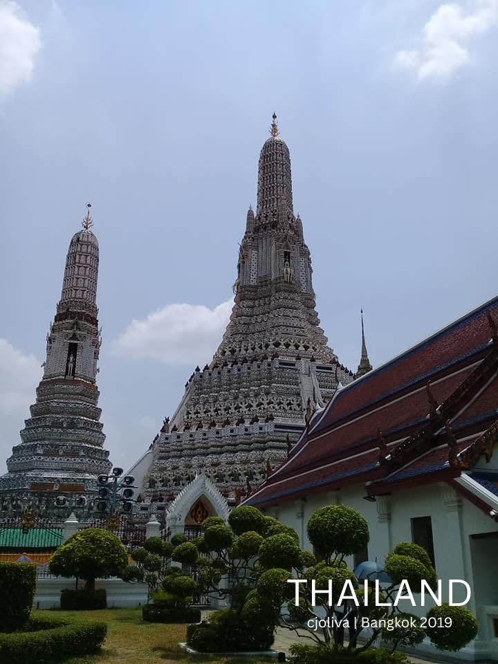 Wide view of Wat Arun temple spires behind a golden royal shrine with yellow decorations.