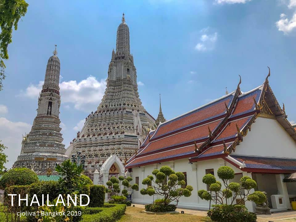 White porcelain towers of Wat Arun temple against a blue sky in Bangkok, Thailand.