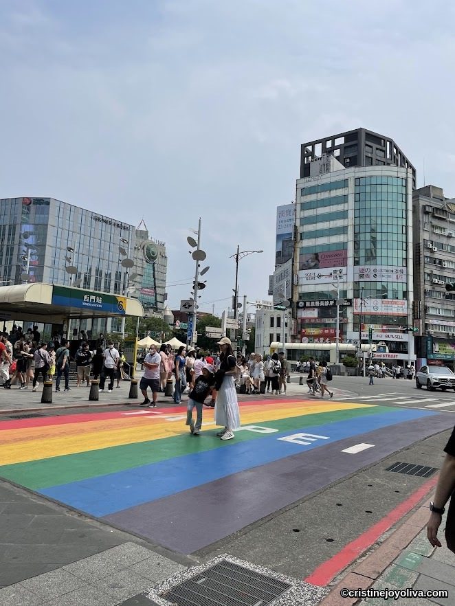 Rainbow crosswalk at Ximen Station in Taipei with pedestrians and modern city buildings