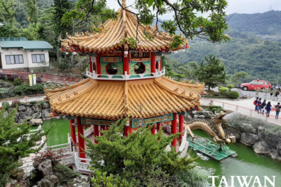 Zhinan Temple pavilion in Taipei with a golden roof, red columns, and a dragon pond surrounded by greenery