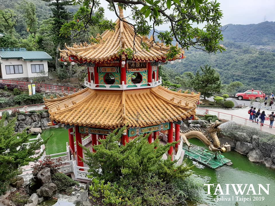 Zhinan Temple pavilion in Taipei with a golden roof, red columns, and a dragon pond surrounded by greenery