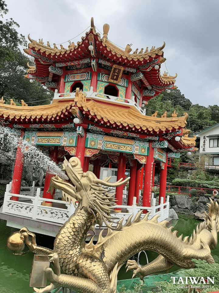 Zhinan Temple pavilion in Taipei with golden roof, red columns, and dragon fountain statue