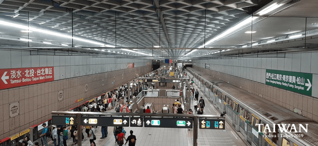 Taipei underground metro station with trains, passengers, and bilingual signage.