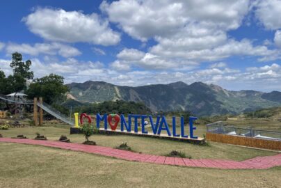 Scenic outdoor view of Montevalle with large colorful letters spelling "I Love Montevalle," including a strawberry shape, surrounded by green hills and mountains under a partly cloudy blue sky.