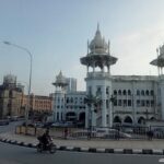 Kuala Lumpur Railway Station with white Mughal-style domes, ornate arches, and a motorcyclist riding along the curved road in front.