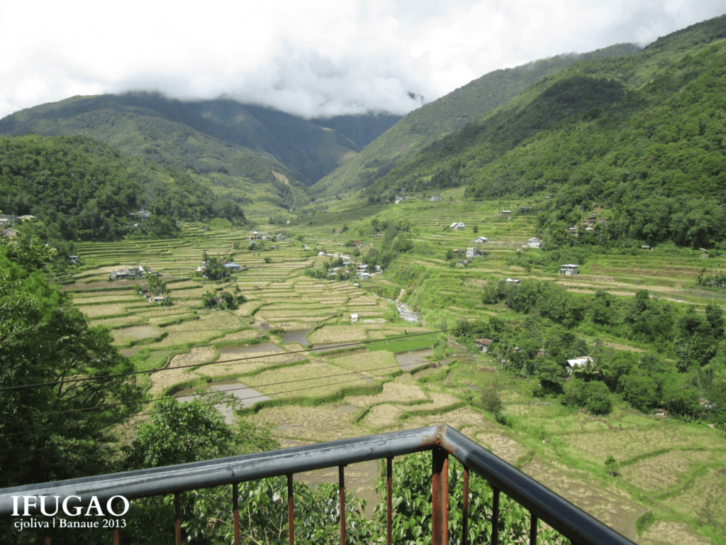 Balcony viewpoint overlooking a wide valley filled with green rice terraces and cloudy mountain peaks in Banaue.