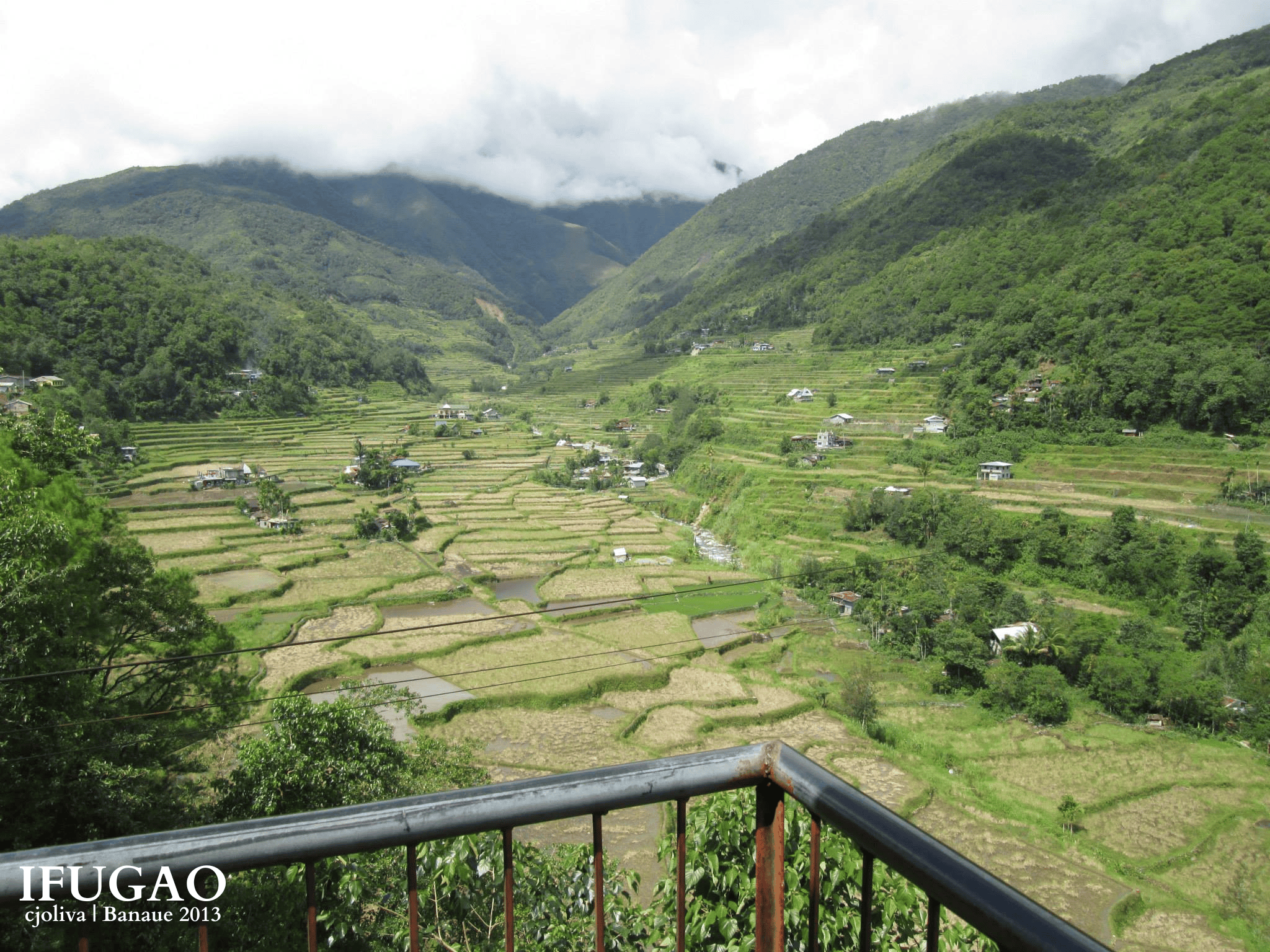 Balcony viewpoint overlooking a wide valley filled with green rice terraces and cloudy mountain peaks in Banaue.