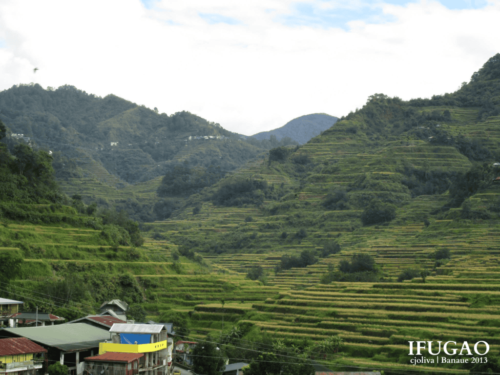 Overview of Banaue town buildings nestled at the base of expansive green mountain rice terraces in Ifugao.