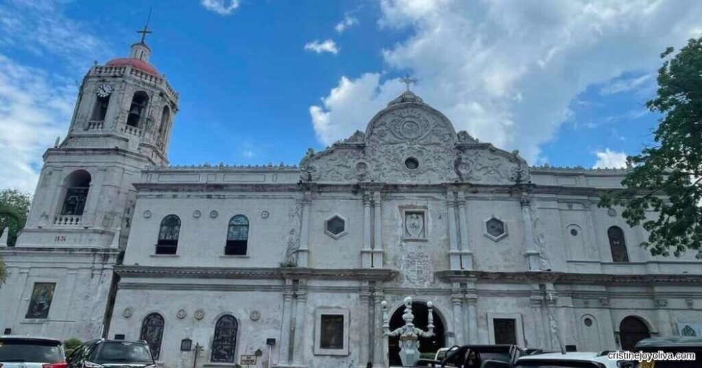 A front view of Cebu Metropolitan Cathedral showing its detailed stone facade and bell tower under a partly cloudy blue sky