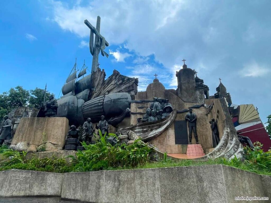 Detailed view of the Heritage of Cebu Monument featuring sculptures of historical figures, a ship, and crosses against a partly cloudy sky