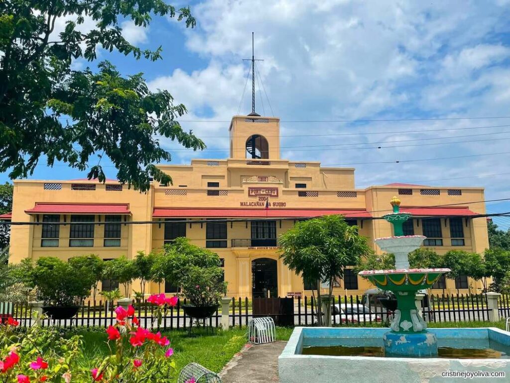 Yellow historic building of the National Museum of the Philippines in Cebu City with a garden and fountain in front under a partly cloudy sky