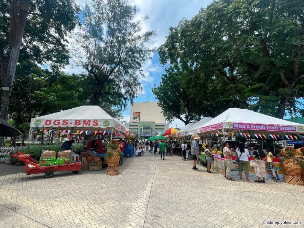 Outdoor market stalls and festival booths at Plaza Sugbo with people browsing under a partly cloudy blue sky