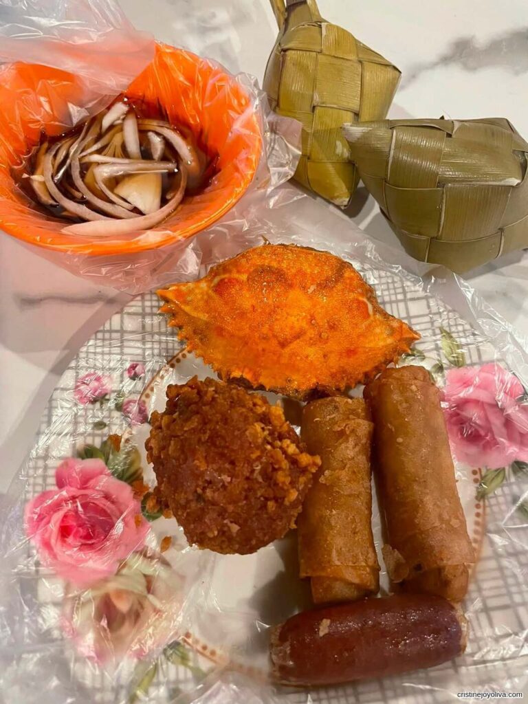 Classic Filipino pungko-pungko meal with fried spring rolls, fried chicken, crab shells, vinegar dipping sauce with onions, and wrapped rice cakes