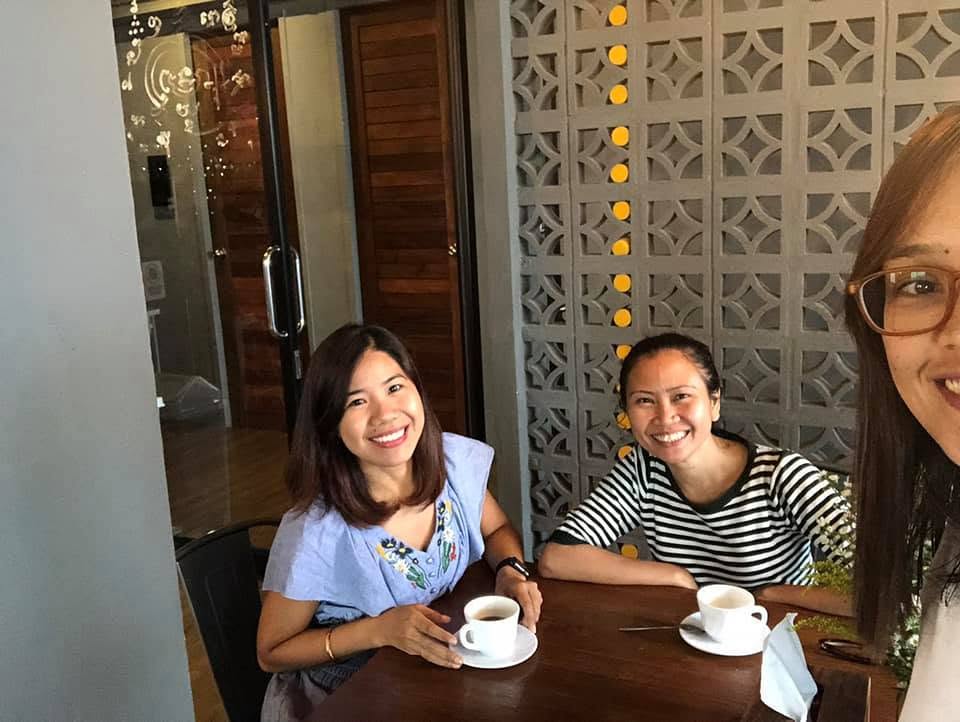 Three smiling friends sitting at a table with coffee cups inside Silom Space coworking area in Bangkok