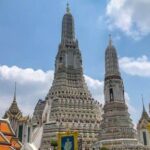 Wat Arun temple with detailed spires standing tall under blue sky in Bangkok, Thailand