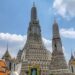 Wat Arun temple with detailed spires standing tall under blue sky in Bangkok, Thailand