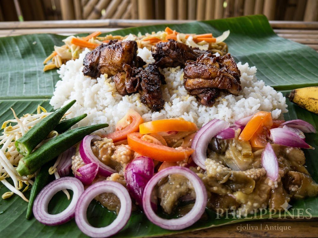 Filipino boodle fight meal on a banana leaf featuring adobo chicken, rice, and fresh ensaladang talong in Antique, Philippines