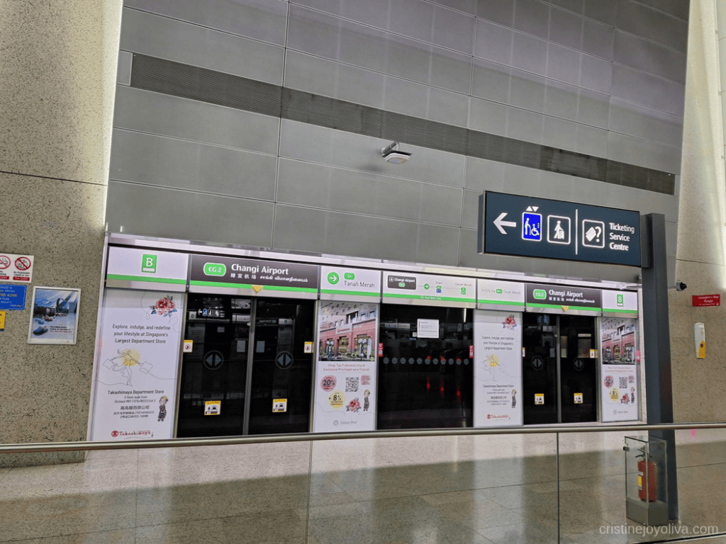 Changi Airport MRT station platform screen doors with overhead directional signs for Tanah Merah and the Ticketing Service Centre.