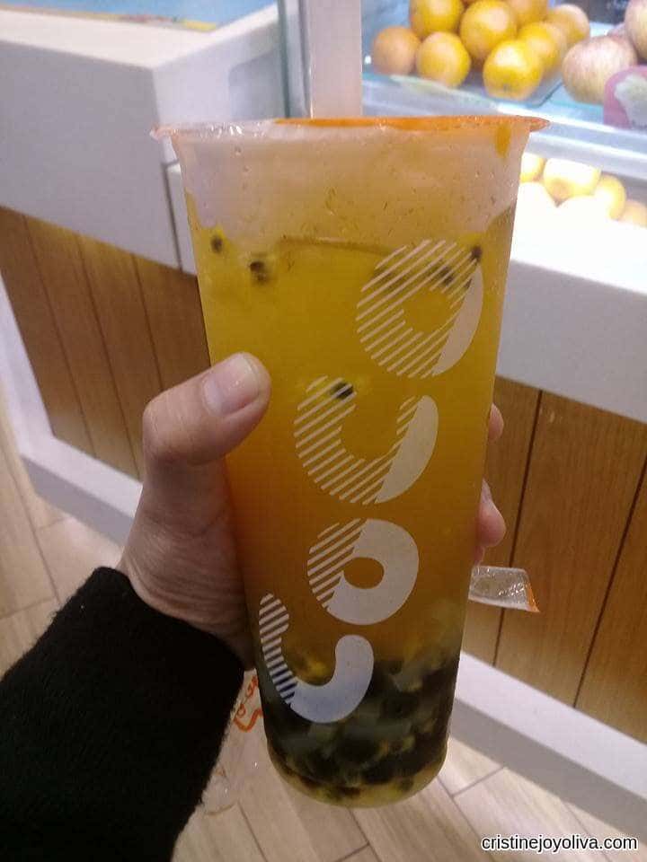 Hand holding a plastic cup of yellow passion fruit tea with tapioca boba and seeds from CoCo Fresh Tea & Juice.