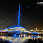 Night view of the Great Harbor Bridge (Dagang Bridge) in Kaohsiung, Taiwan. The white cable-stayed bridge is illuminated in blue, reflecting on the water near Pier-2.