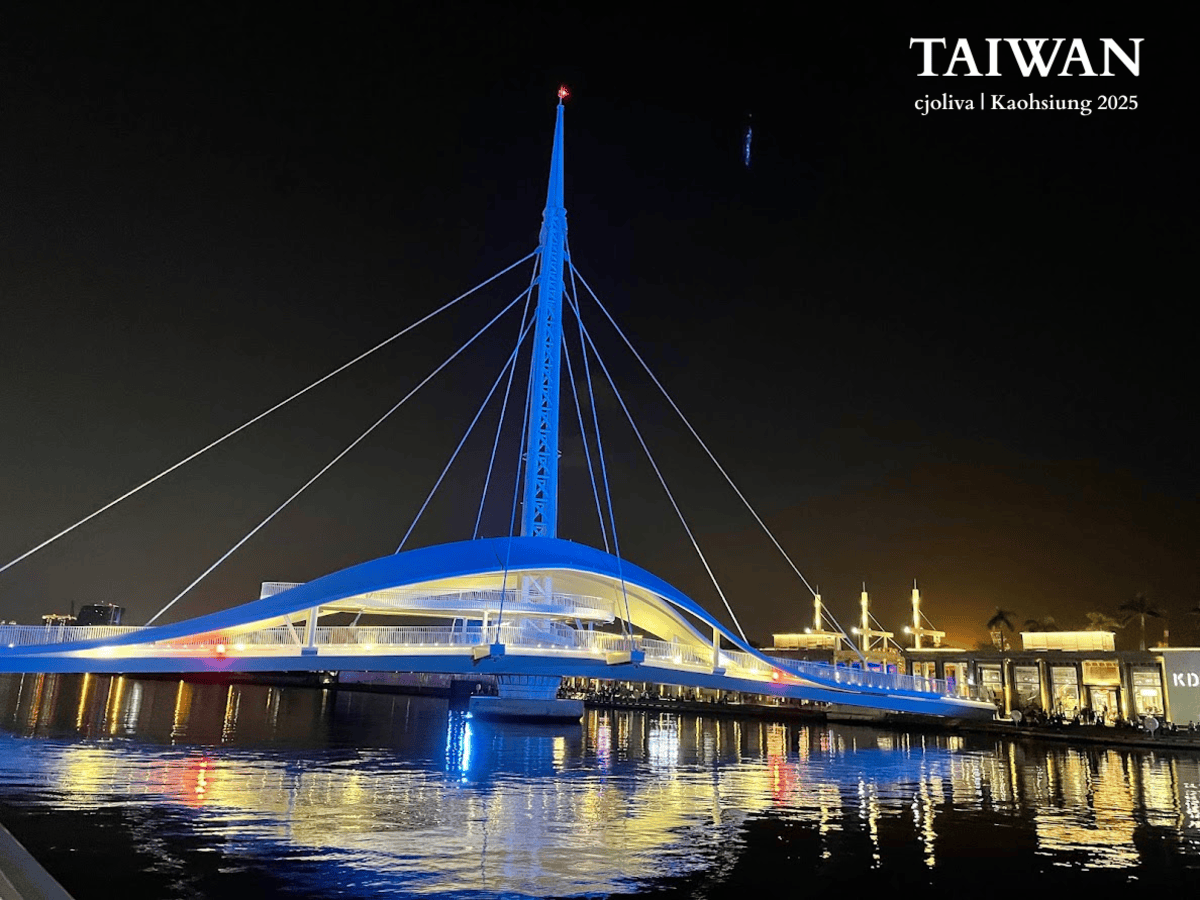 Night view of the Great Harbor Bridge (Dagang Bridge) in Kaohsiung, Taiwan. The white cable-stayed bridge is illuminated in blue, reflecting on the water near Pier-2.