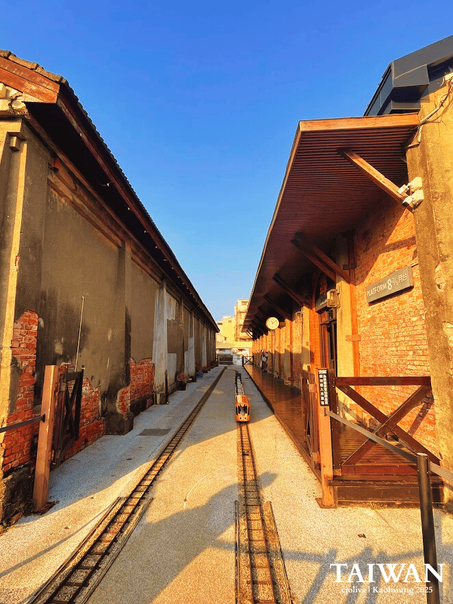 A miniature orange train running along narrow tracks between historic red brick warehouses at Platform 8 of the Hamasen Museum of Taiwan Railway.