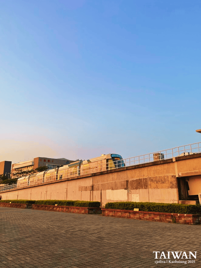 Modern Kaohsiung Light Rail transit train moving along an elevated track against a clear blue sky in Taiwan during golden hour.