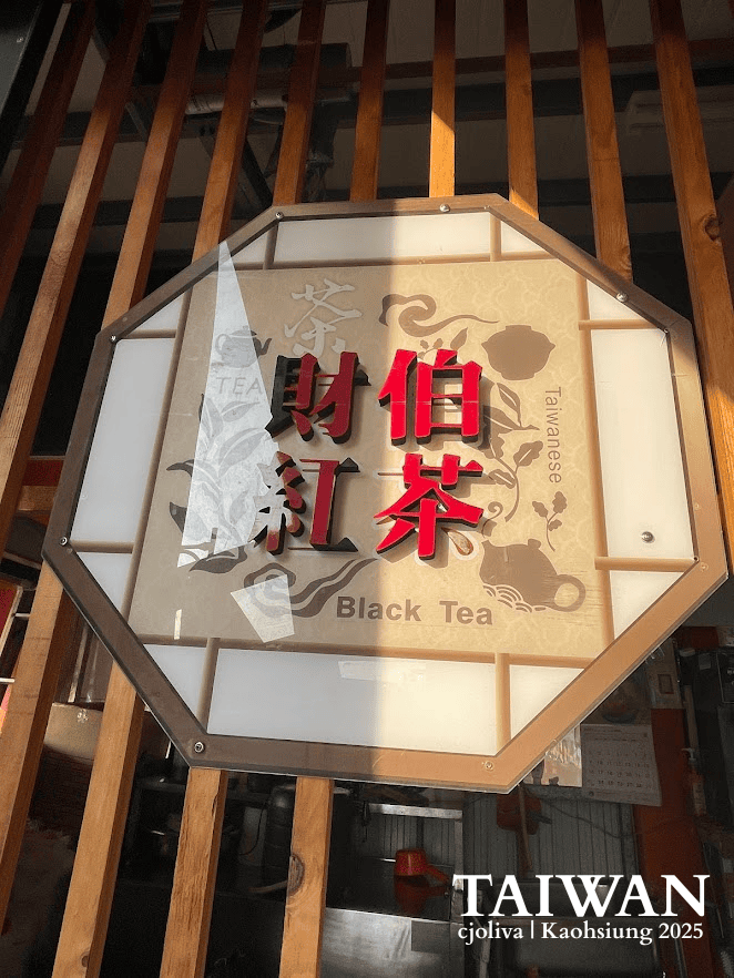 An octagonal Taiwanese tea shop sign with bold red Chinese characters, English text “Black Tea,” and teapot illustrations on a wooden wall.