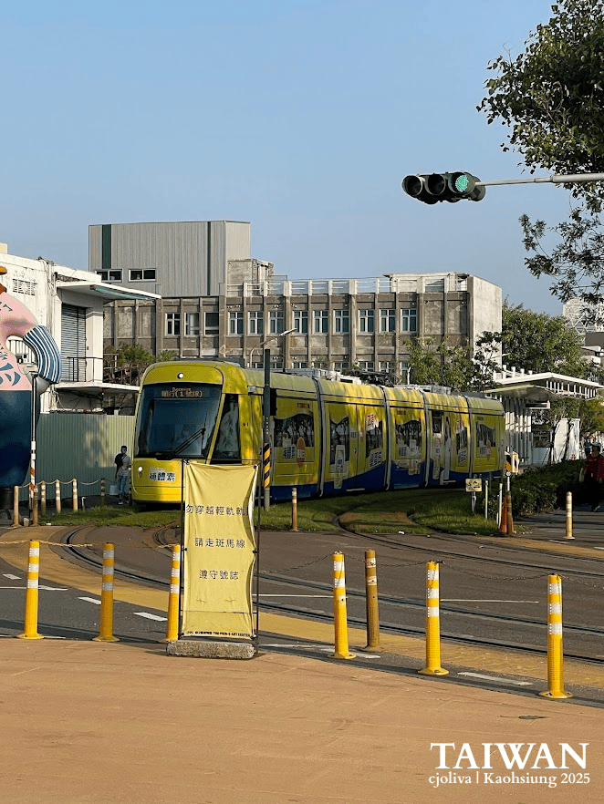 Yellow Kaohsiung Light Rail Transit train navigating a street curve near Pier-2 Art Center.