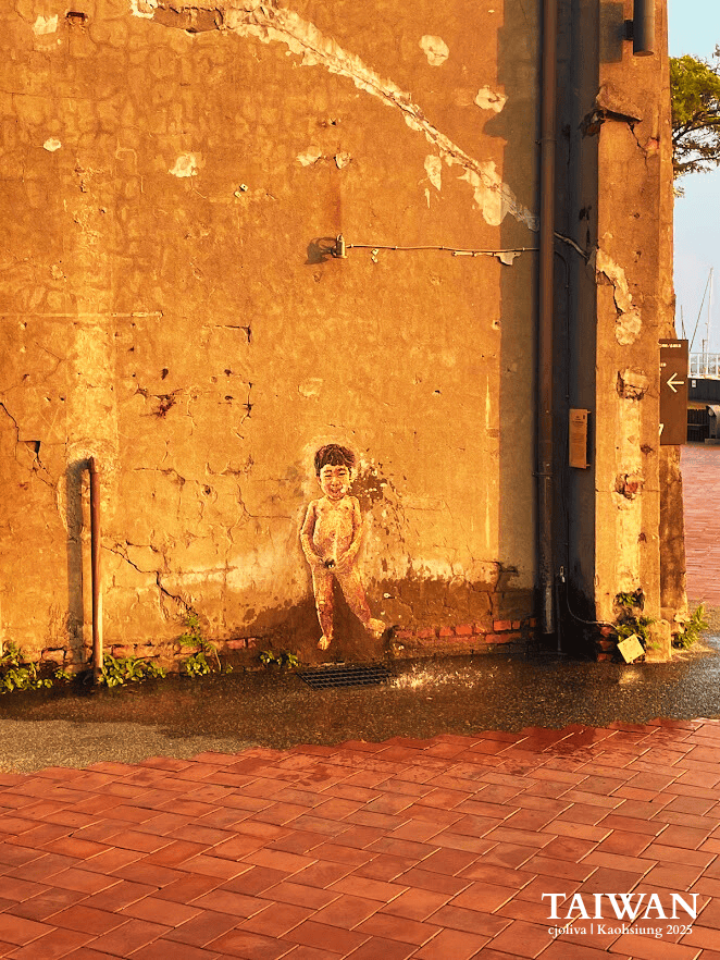 Playful street art installation of a peeing boy spurting water onto the pavement at Pier-2 Art Center