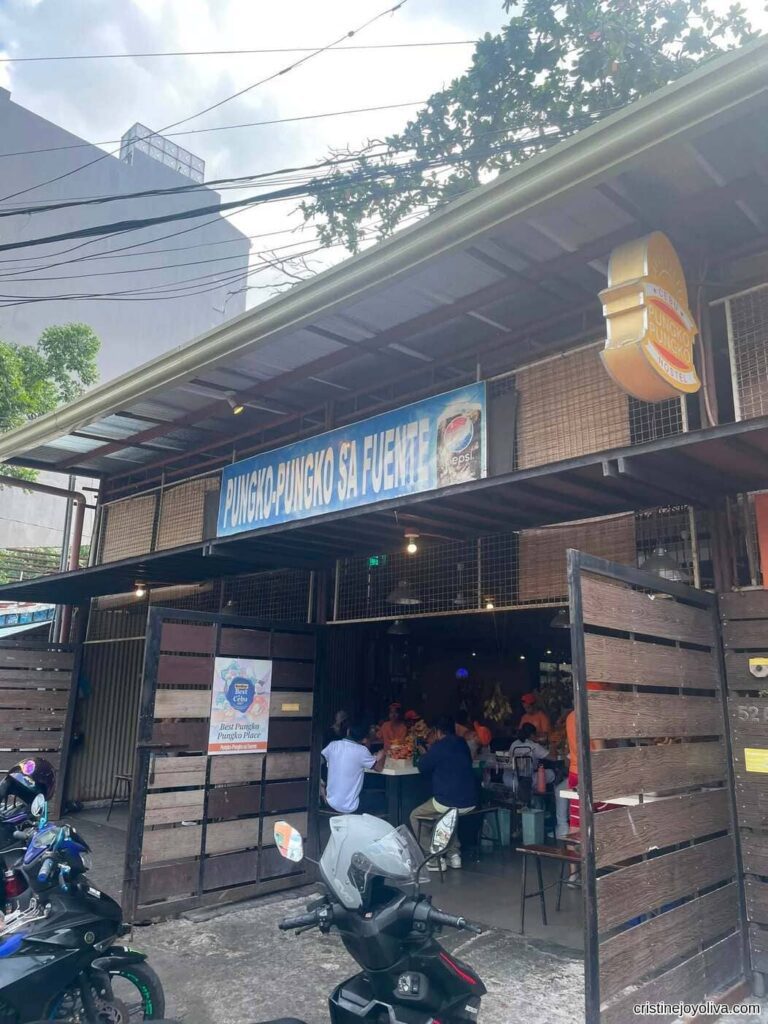 Storefront entrance of Pungko-Pungko sa Fuente in Cebu City showing open wooden gates, a blue sign overhead, parked motorcycles, and customers dining inside.