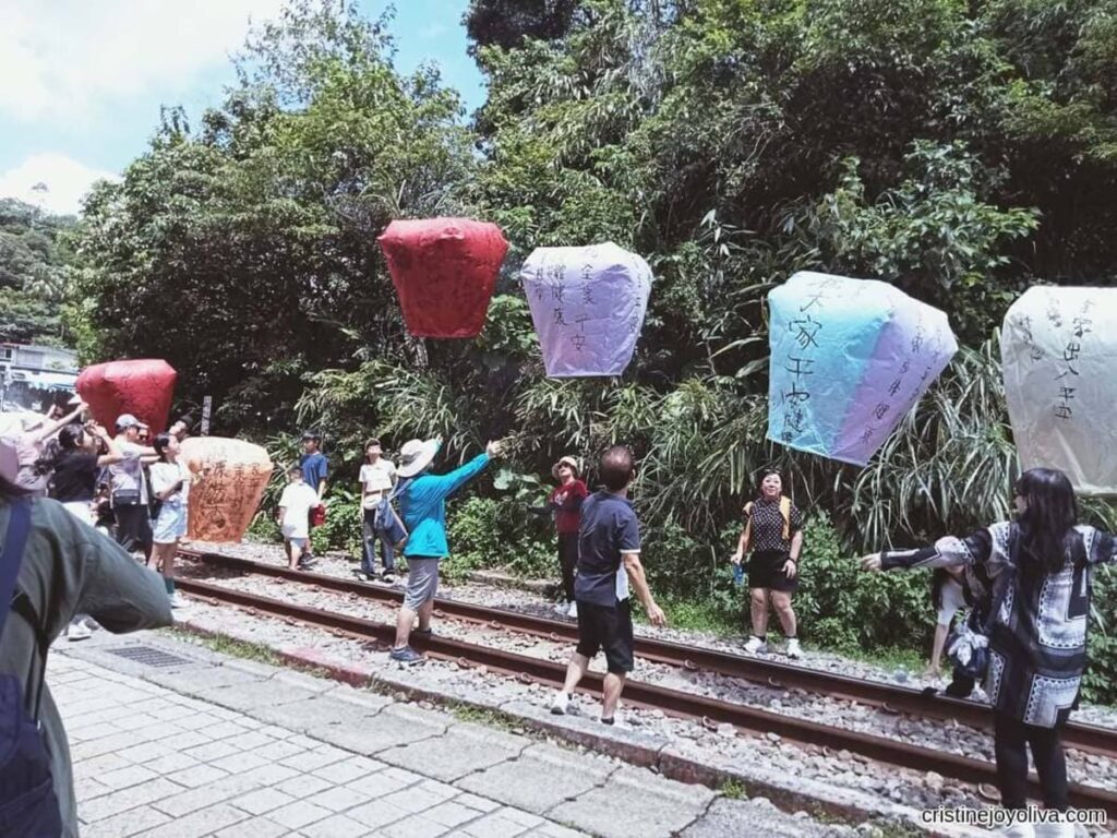 Travelers on the Pingxi Line itinerary release colorful sky lanterns inscribed with handwritten wishes over the railway tracks in Pingxi, Taiwan.