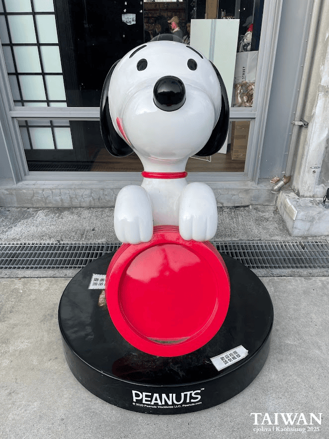 Large white Snoopy statue with a red bowl standing on a round black Peanuts base outside a shop at Pier-2 Art Center.
