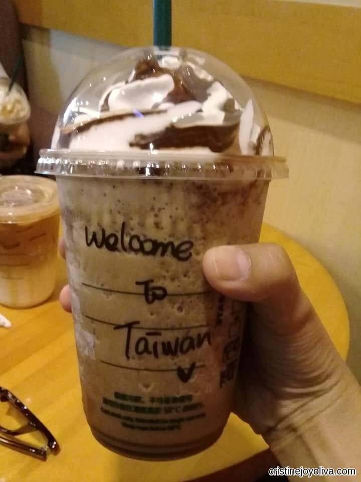 Hand-holding a Starbucks cold drink with whipped cream and chocolate drizzle, labeled "Welcome to Taiwan."