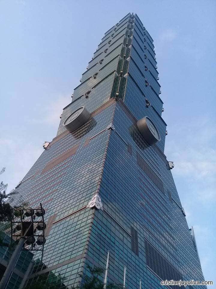 Low-angle view looking straight up at the blue glass and stacked segments of the Taipei 101 skyscraper.