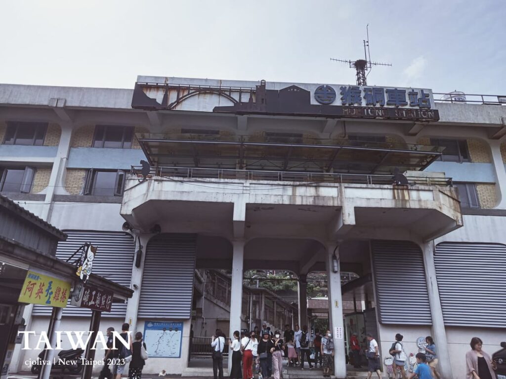The weathered exterior of Houtong Station, Taiwan, with crowds at the entrance and a cat silhouette on the railing.