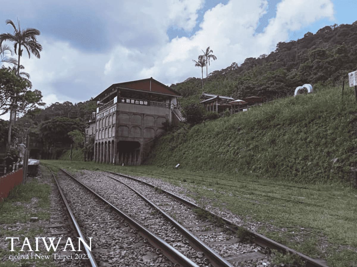 Railway tracks curving past a multi-story building with an observation deck café on a green hillside near Jingtong, Taiwan.