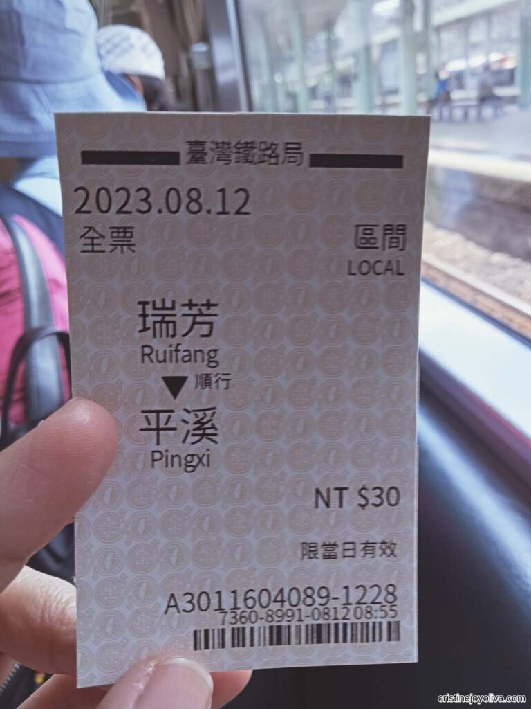 A hand holding a Taiwan Railway ticket from Ruifang to Pingxi, priced at NT$30, with train tracks visible through the window.