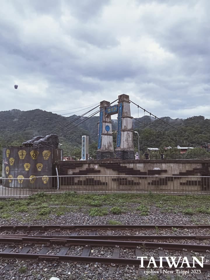 The weathered Jingan Suspension Bridge over railway tracks in Shifen, Taiwan, with mountains in the background.