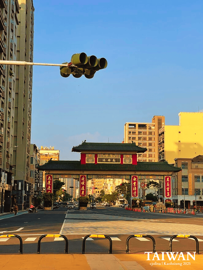 Large traditional Chinese-style green and red ceremonial gate standing over a wide city street in Kaohsiung during the golden hour.