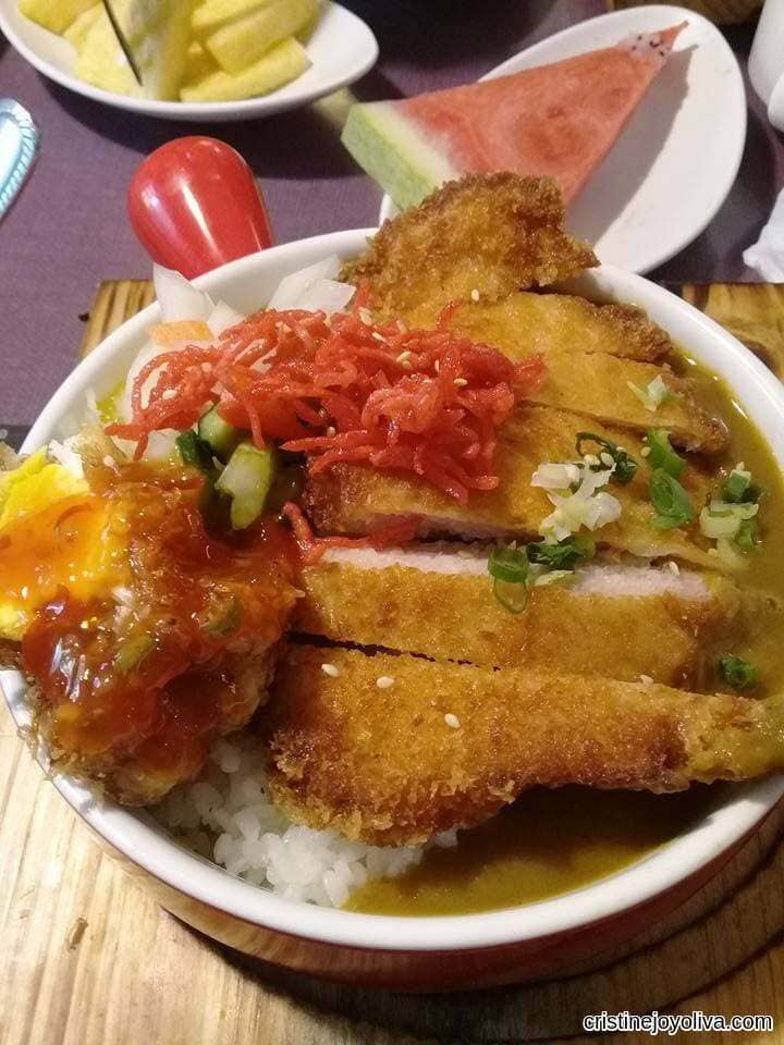 Sliced deep-fried pork cutlet over steamed white rice and Japanese curry sauce in a red-handled bowl.