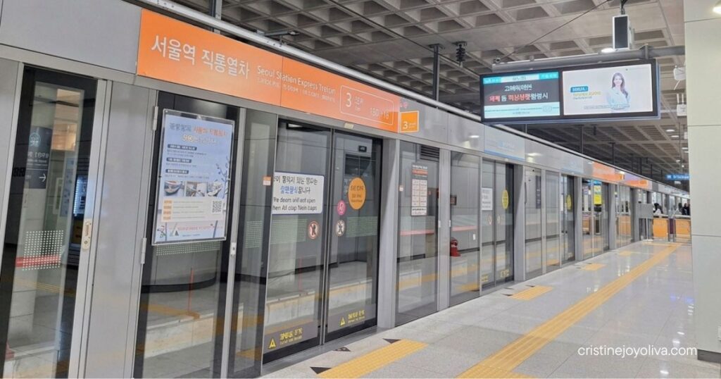 An empty train platform with screen doors and orange signage for the Seoul Station Express Train.