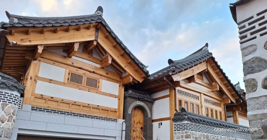A traveler walks past a beautiful, modern-renovated traditional Korean hanok house with wooden beams and a stone wall in Bukchon Hanok Village.