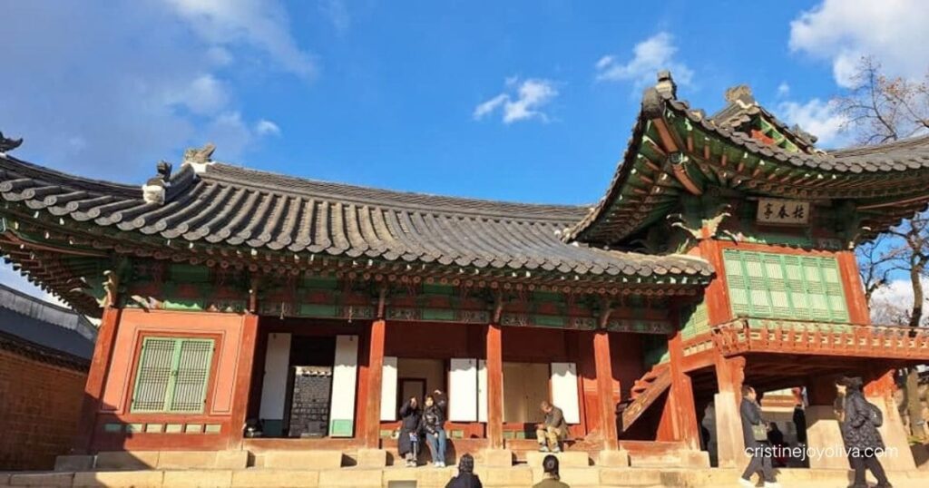 Seongjeonggak Hall at Changdeokgung Palace features a unique two-story wooden pavilion wing under a bright blue sky.