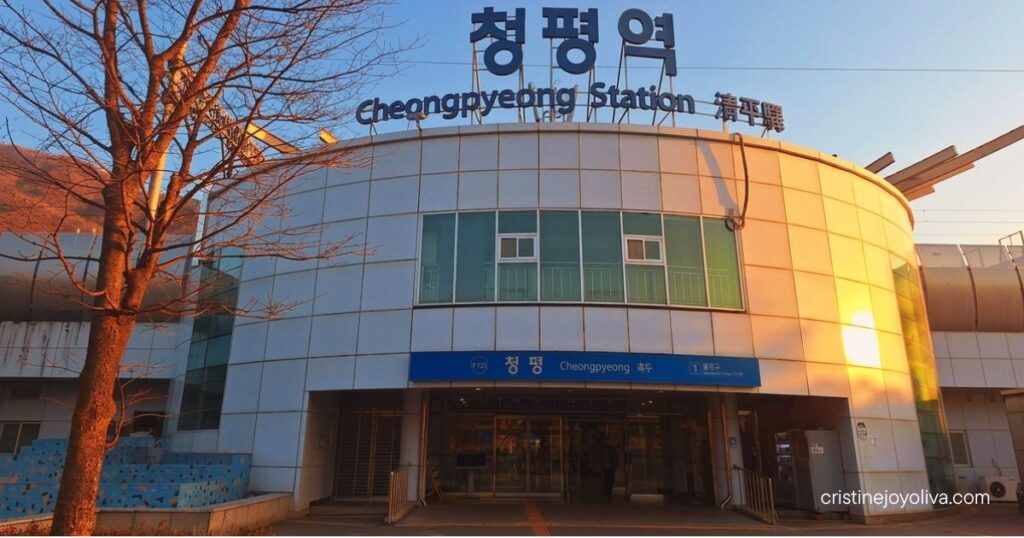 Warm late-afternoon sunlight glows against the curved exterior of Cheongpyeong Station beside a bare winter tree.
