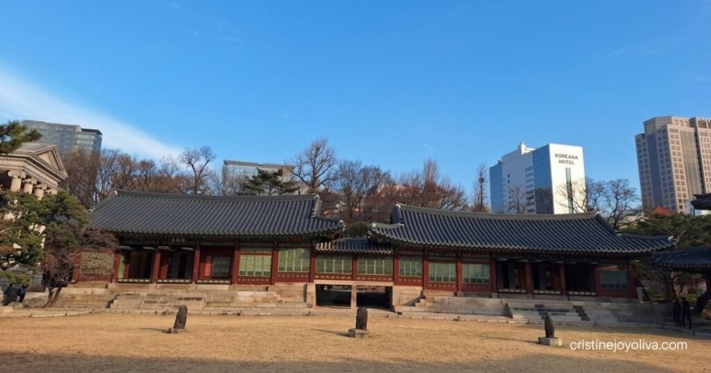 Wide view of Deoksugung Palace's traditional hanok hall with Seoul's skyline in the background