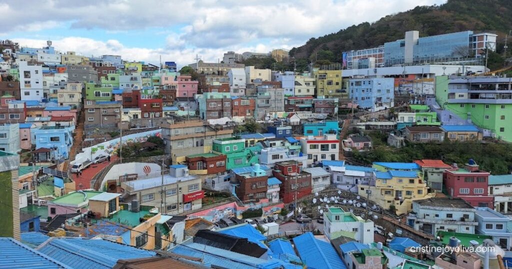 High-angle view of colorful pastel houses on a steep hillside under a blue sky in Gamcheon Culture Village, Busan.