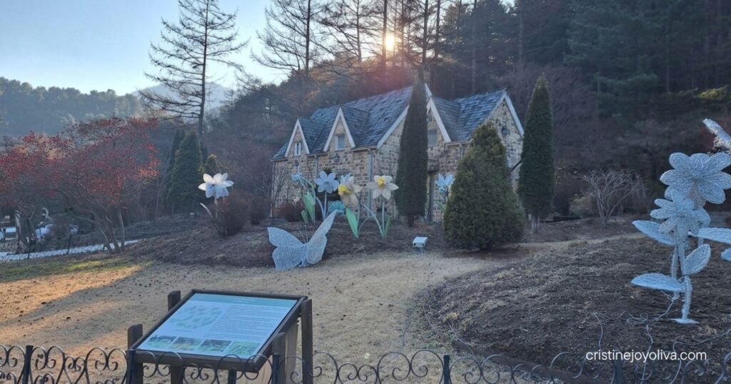 Large flower and butterfly light sculptures sit in front of a European-style stone cottage at the Garden of Morning Calm