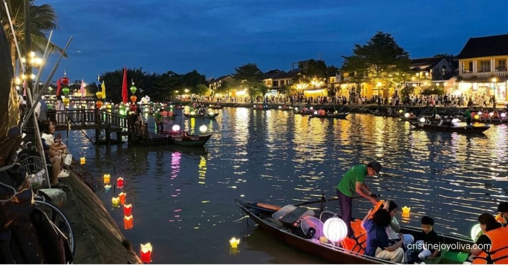 Wooden sampan boats decorated with glowing lanterns sail along the reflective Thu Bon River in Hoi An at dusk.