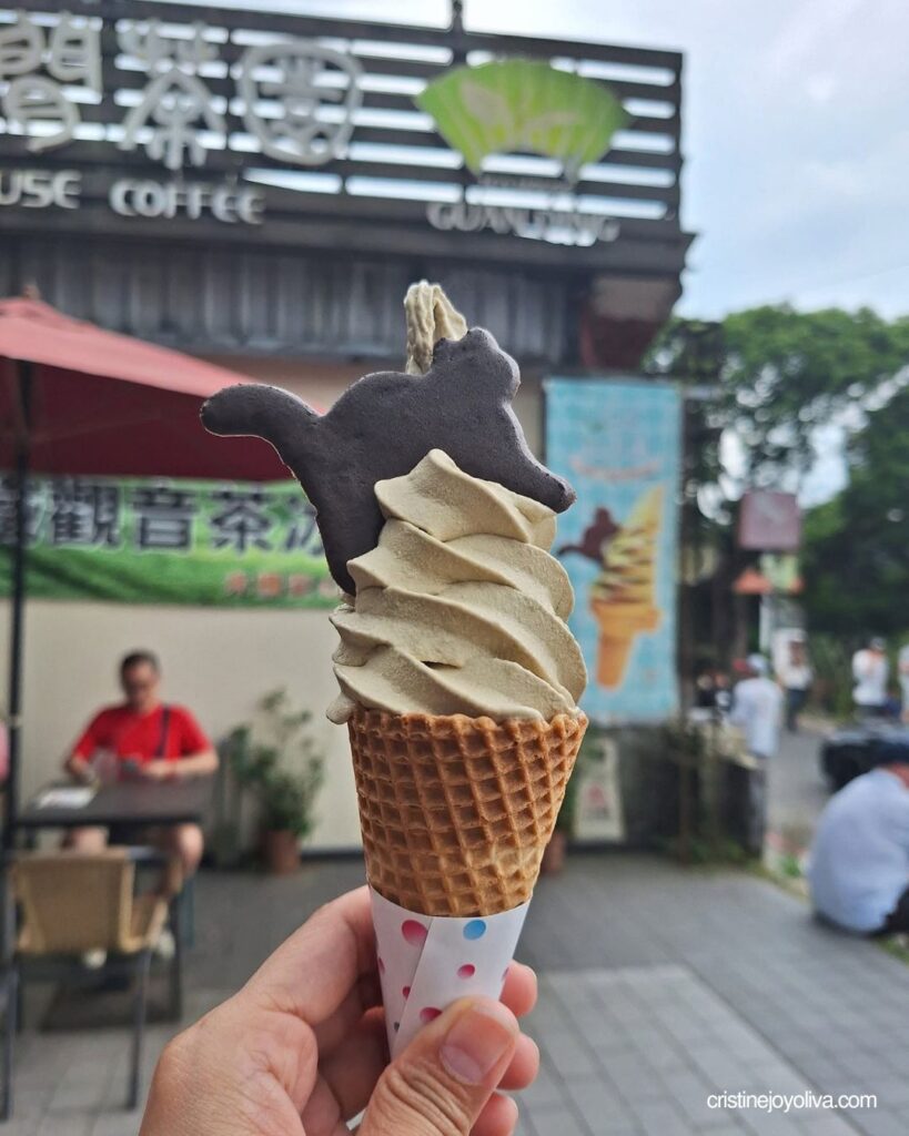 A hand holds a green tea soft serve cone topped with a cat cookie in Maokong.
